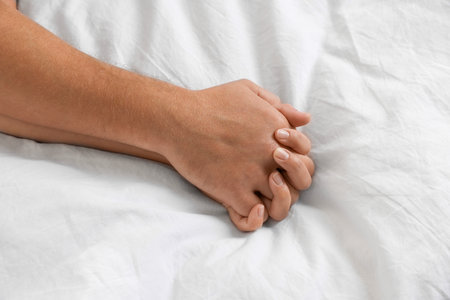 Lovely couple holding hands in bed, top viewの写真素材