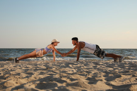 Sporty couple doing exercise on beach at sunsetの写真素材