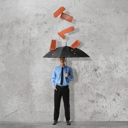 Businessman protecting himself from falling bricks with umbrella on grey textured backgroundの写真素材