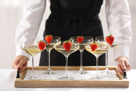 Waiter holding tray with glasses of champagne indoors, closeup
