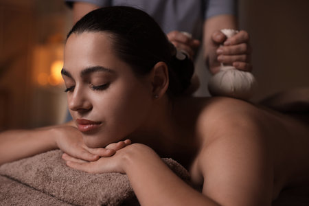 Woman receiving back massage with herbal bags in spa salonの写真素材
