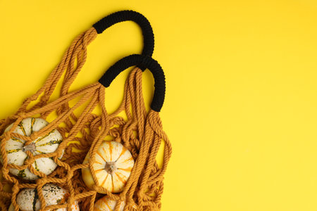 Macrame shopping bag with pumpkins on yellow background, top view. Space for textの写真素材