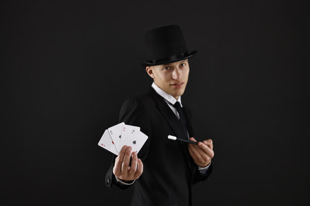 Illusionist pointing magic wand on playing cards against black background, selective focusの写真素材