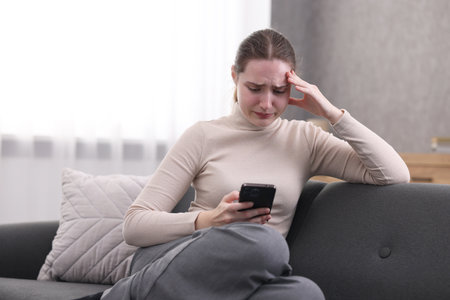 Depressed woman calling hotline for mental health help on sofa at home