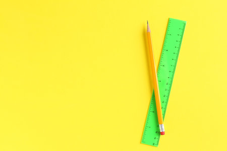 Ruler and pencil on yellow background, top view. Space for text