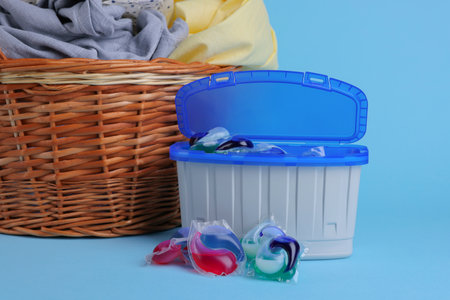 Detergent capsules and laundry basket on light blue background