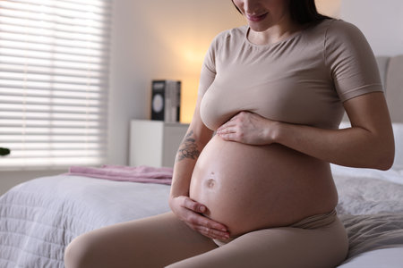 Pregnant woman with cute belly on bed at home, closeup