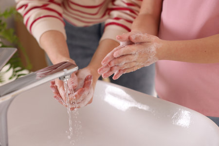 Mother and daughter washing their hands above sink indoors, closeupの写真素材