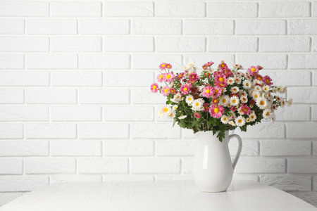 Vase with beautiful flowers on wooden table near white brick wall, space for textの写真素材