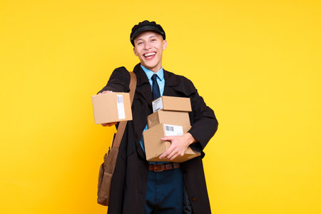 Happy postman with bag giving parcel on yellow backgroundの写真素材