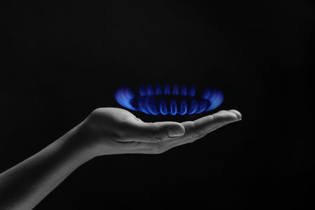Woman holding gas burner with blue flame on black background, closeup.の写真素材