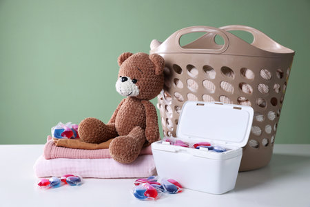 Detergent capsules, clean linens, teddy bear and laundry basket on white tableの写真素材