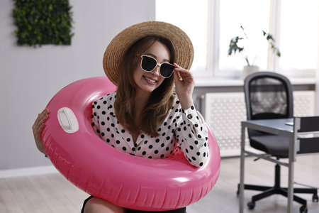 Businesswoman with inflatable ring, straw hat and sunglasses in officeの写真素材