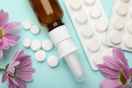 Allergy treatment. Nasal spray, pills and flowers on light blue background, flat lay