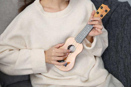 Woman playing ukulele in armchair at home, closeup