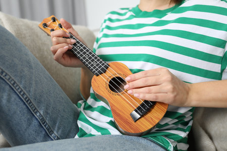 Woman playing ukulele on sofa at home, closeupの写真素材
