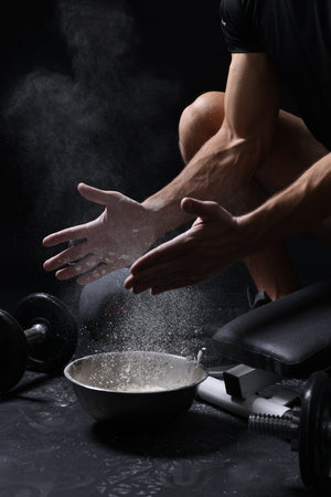 Man clapping hands with talcum powder above bowl before training on black background, closeupの写真素材