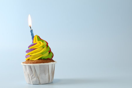 Tasty cupcake with colorful cream and burning candle on light blue background, space for textの写真素材