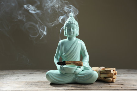 Smoldering palo santo stick and Buddha statue on wooden table against grey backgroundの写真素材