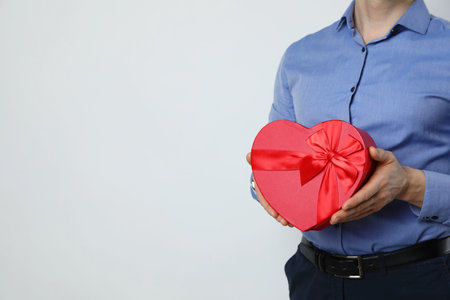 Happy Valentine's Day. Man with heart shaped gift box on white background, closeup. Space for textの写真素材