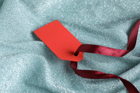 Blank tag with ribbon on teal fabric, closeup