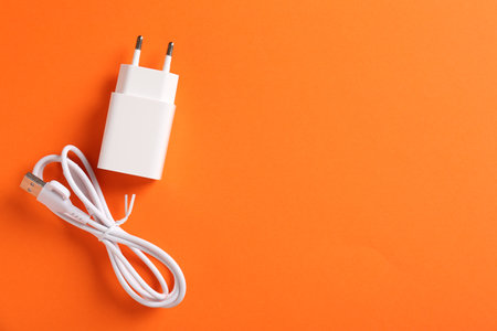 USB power adapter and charge cable on orange background, flat lay. Space for text