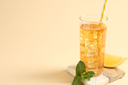 Refreshing iced tea with drinking straw in glass, mint and slice of lemon on beige background, closeup. Space for textの写真素材