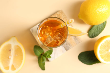 Refreshing iced tea with drinking straw in glass, mint and lemon on beige background, flat layの写真素材