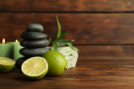 Spa composition with fresh limes, pebble stones and burning candles on wooden table, closeup. Space for textの写真素材