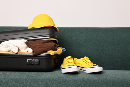 Open suitcase full of different messy clothes and sneakers on sofa indoorsの写真素材