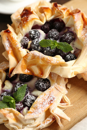 Tasty puff pastries with blueberries, powdered sugar and mint on table, closeup