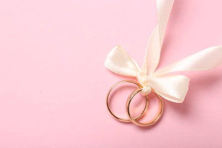 Wedding rings tied with ribbon on pink background, top viewの写真素材