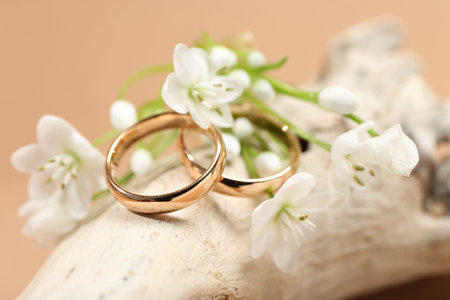 Wedding rings and beautiful flowers on piece of decorative wood against beige background, closeupの写真素材