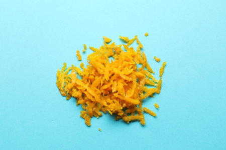 Pile of fresh orange zest on light blue background, top view