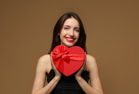 Happy Valentine's Day. Beautiful woman with heart shaped gift box on brown backgroundの写真素材