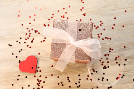 Romantic gift and confetti in shape of hearts on light wooden table, flat lay. Happy Valentine's dayの写真素材