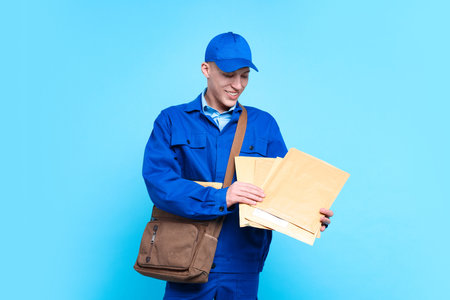 Happy postman with bag and envelopes on light blue backgroundの写真素材