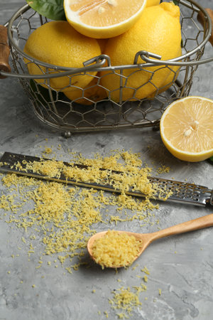 Lemon zest, spoon, grater and fresh fruits on grey textured tableの写真素材