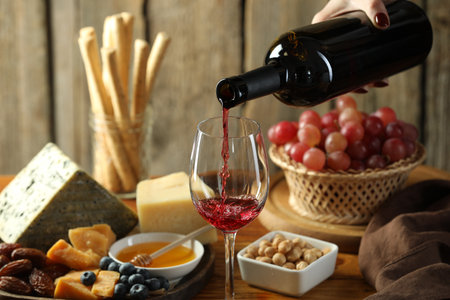 Woman pouring red wine into glass at table with different snacks, closeupの写真素材