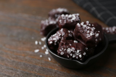 Tasty chocolate candies with salt in bowl on wooden table, closeup. Space for textの写真素材