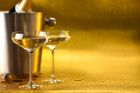 Champagne in glasses and ice bucket with bottle on golden background. Space for textの写真素材