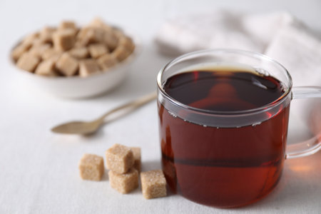 Aromatic black tea in cup and brown sugar cubes on white table, closeupの写真素材