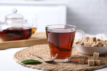 Aromatic black tea in cup and brown sugar cubes on white table, closeupの写真素材