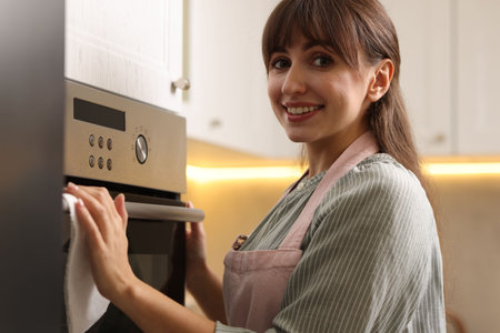 Smiling woman wiping oven with paper towel in kitchenの写真素材