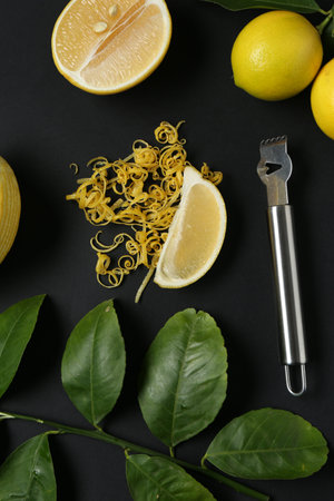 Lemon zest, zester tool, fresh fruits and leaves on black background, flat lay