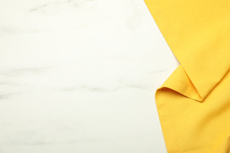 Yellow tablecloth on white marble background, top view. Space for textの写真素材