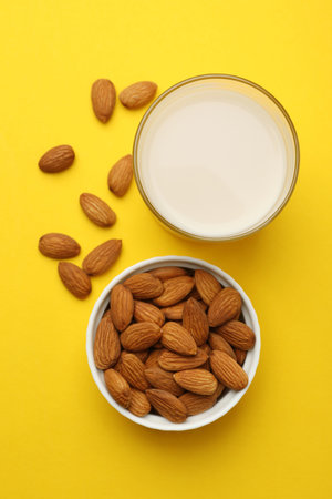 Fresh nut milk in glass and almonds on yellow background, flat layの写真素材