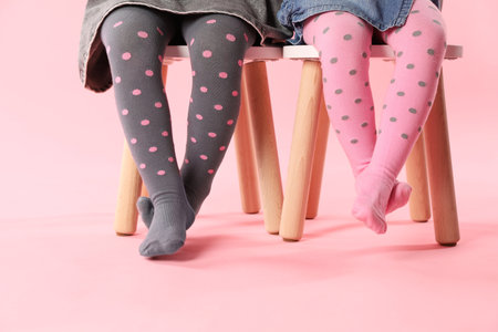 Kids wearing tights on stools against pink background, closeup