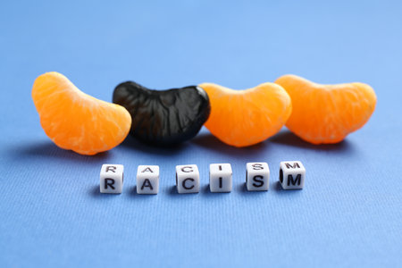 Word Racism and tangerine segments of different colors on blue background, closeupの写真素材
