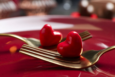 Romantic table setting for Valentine's day. Forks with decorative hearts on red plate, closeup